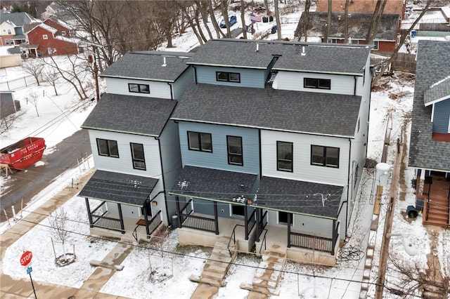 snow covered rear of property with a shingled roof and fence