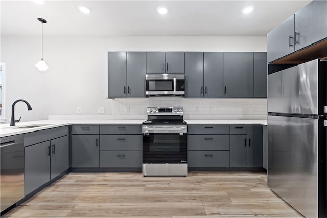 kitchen featuring decorative backsplash, light wood-style flooring, stainless steel appliances, gray cabinetry, and a sink