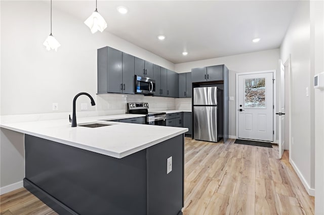 kitchen featuring stainless steel appliances, a peninsula, a sink, light countertops, and tasteful backsplash