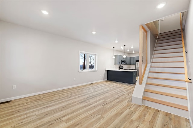 unfurnished living room with recessed lighting, visible vents, baseboards, stairs, and light wood-type flooring