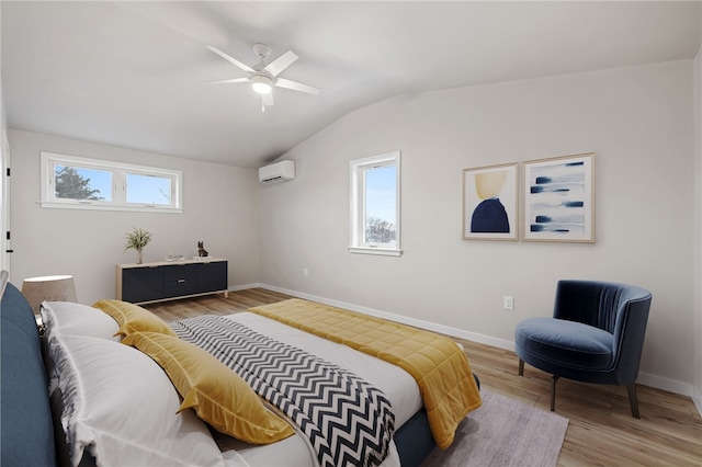 bedroom with vaulted ceiling, a wall unit AC, light wood-style flooring, and baseboards