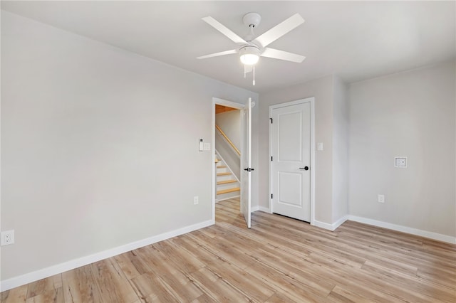 spare room with light wood-style floors, ceiling fan, baseboards, and stairs