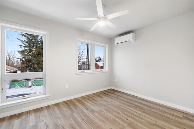 spare room featuring a ceiling fan, light wood-type flooring, an AC wall unit, and baseboards