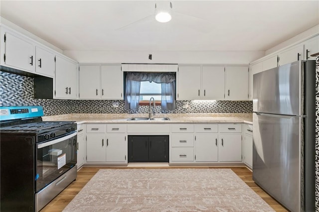 kitchen with light wood finished floors, white cabinets, appliances with stainless steel finishes, light countertops, and a sink