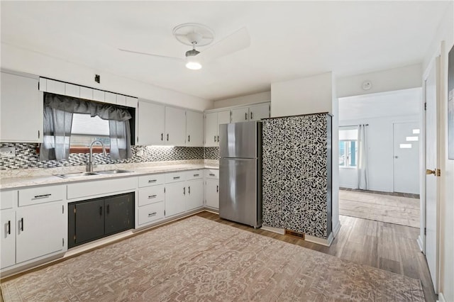 kitchen featuring light wood finished floors, tasteful backsplash, freestanding refrigerator, light countertops, and a sink