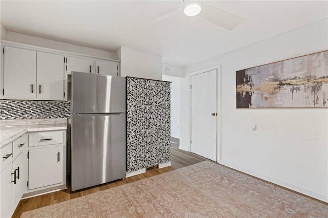 kitchen featuring light wood-type flooring, backsplash, freestanding refrigerator, and white cabinets