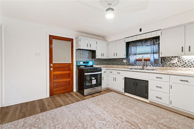 kitchen featuring white cabinets, stainless steel range with gas stovetop, backsplash, light wood-type flooring, and a sink