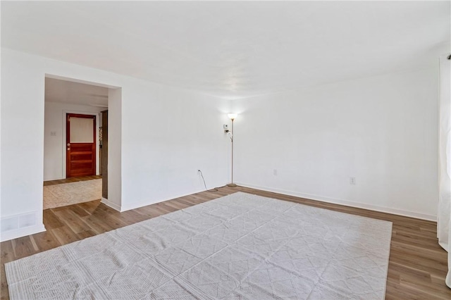 empty room featuring wood finished floors, visible vents, and baseboards