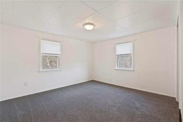 empty room with dark colored carpet, plenty of natural light, a paneled ceiling, and baseboards