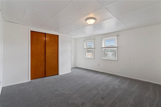 unfurnished bedroom featuring baseboards, dark carpet, and a closet