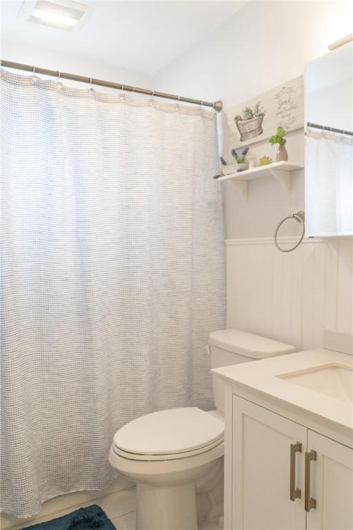 full bath with tile patterned flooring, toilet, vanity, and a wainscoted wall