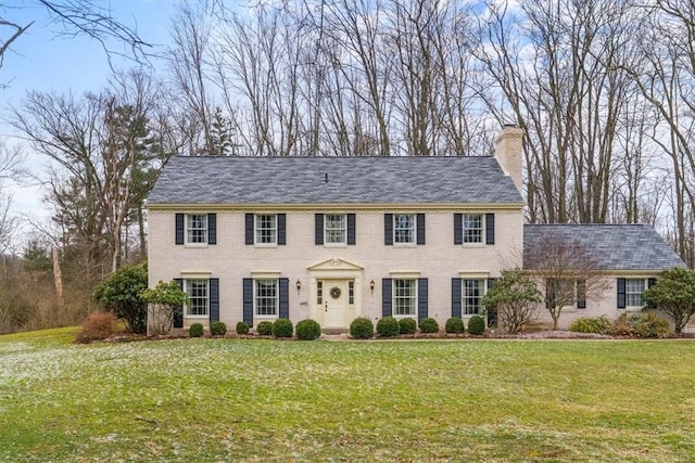 colonial house with a front yard, brick siding, and a chimney