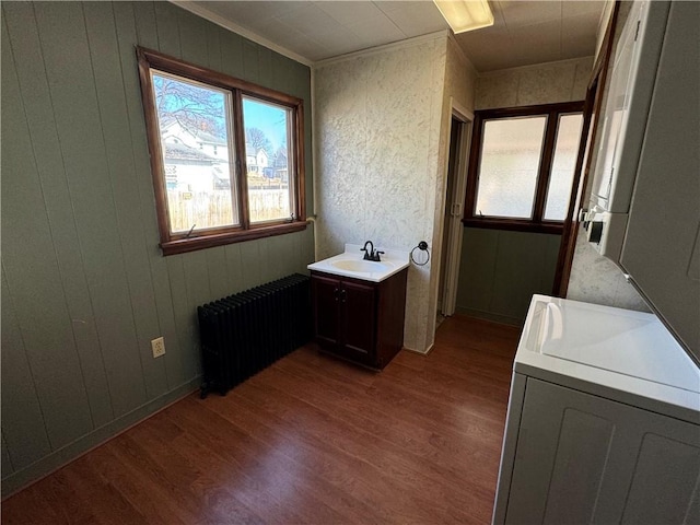 bathroom with wood finished floors, a sink, washer / dryer, and radiator