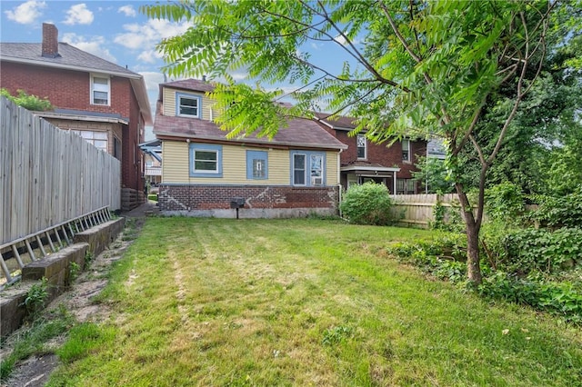 back of house with brick siding, a fenced backyard, and a yard