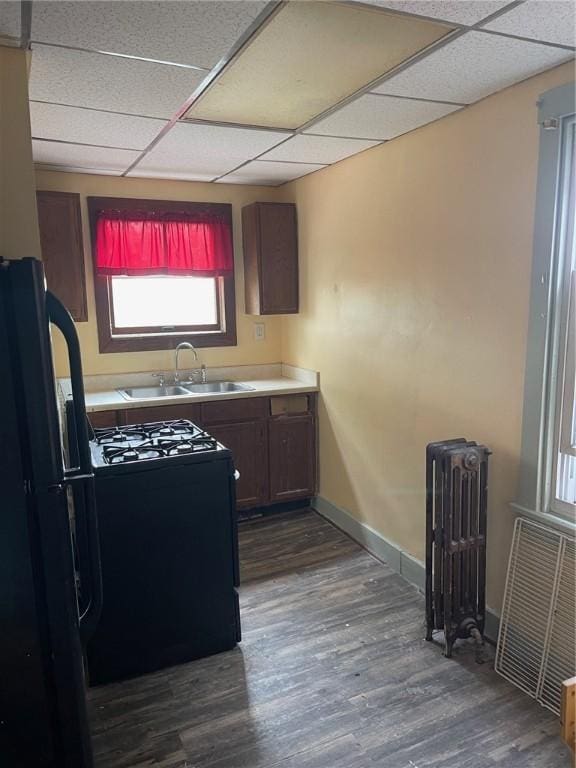 kitchen featuring dark wood-style flooring, radiator heating unit, freestanding refrigerator, a sink, and a drop ceiling