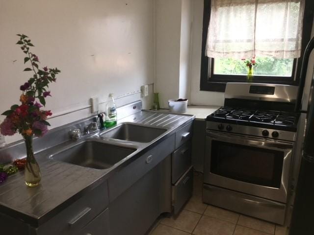 kitchen with a sink, stainless steel gas range oven, and light tile patterned floors