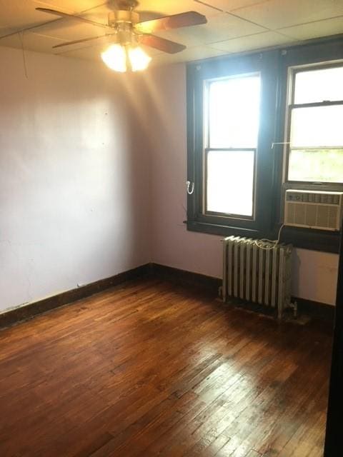 spare room featuring ceiling fan, cooling unit, baseboards, radiator heating unit, and dark wood finished floors