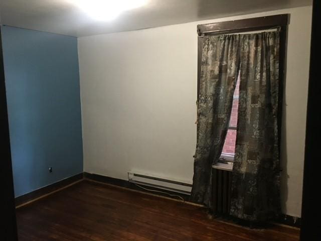 unfurnished room with a baseboard radiator, baseboards, and wood finished floors