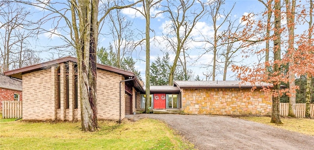 mid-century home with driveway, brick siding, a front yard, and fence