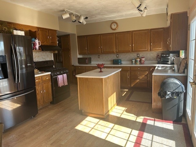 kitchen with light countertops, light wood-type flooring, stainless steel refrigerator with ice dispenser, brown cabinets, and gas stove