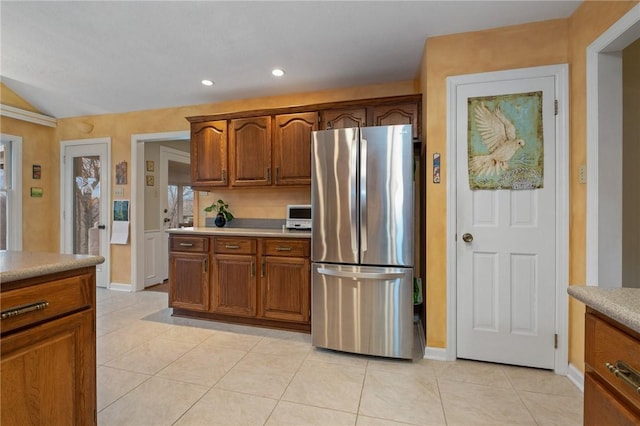 kitchen featuring light tile patterned floors, brown cabinetry, freestanding refrigerator, light countertops, and recessed lighting