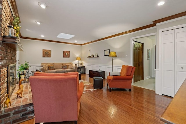 living area featuring crown molding, a wainscoted wall, a fireplace, and wood finished floors