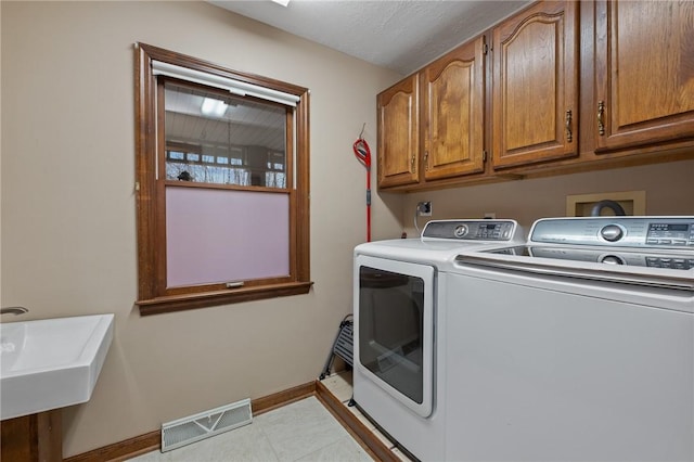 washroom with a sink, visible vents, baseboards, washer and dryer, and cabinet space