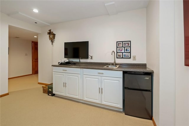 kitchen featuring dark countertops, white cabinetry, a sink, and freestanding refrigerator