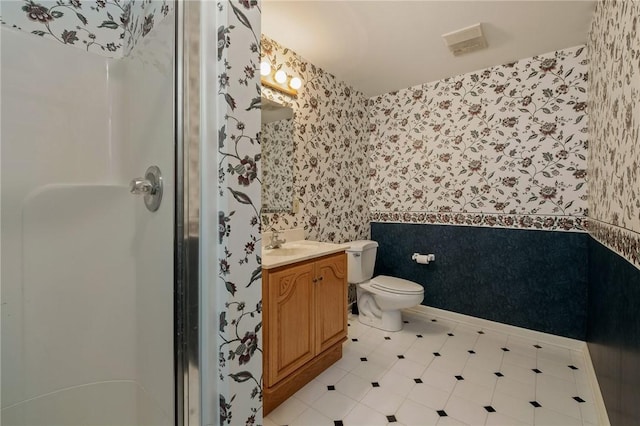 bathroom with toilet, vanity, baseboards, a shower stall, and wallpapered walls