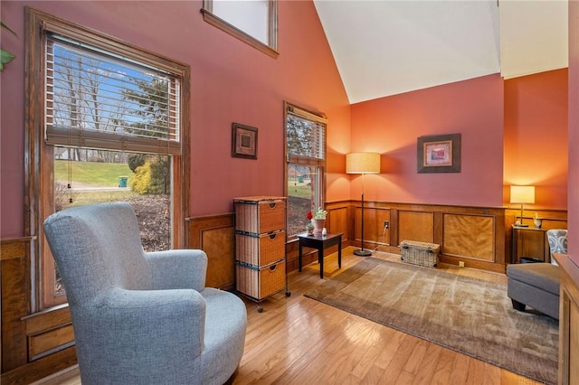 sitting room with a wainscoted wall, wood-type flooring, and high vaulted ceiling