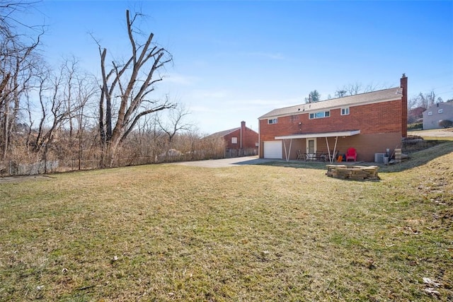 rear view of house with brick siding, a chimney, a lawn, a garage, and driveway