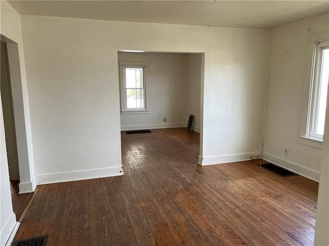 empty room with dark wood-style floors, visible vents, and baseboards