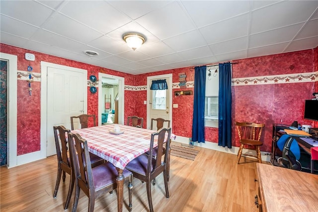 dining space featuring light wood-style floors, visible vents, a drop ceiling, and wallpapered walls