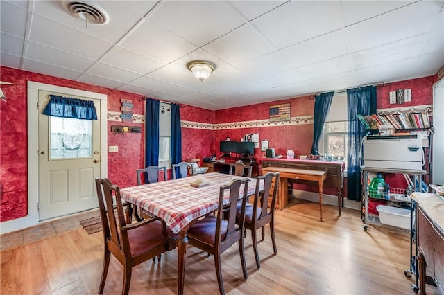 dining room with a drop ceiling, wood finished floors, visible vents, and wallpapered walls