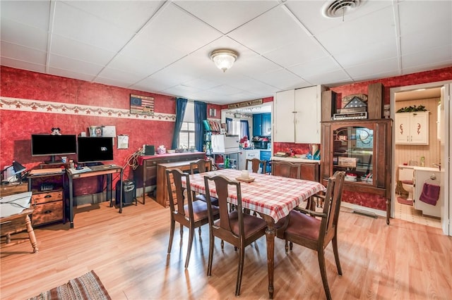 dining space with a paneled ceiling, visible vents, light wood-style flooring, and wallpapered walls