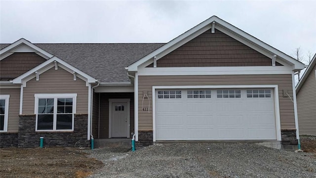 craftsman inspired home with a garage, stone siding, roof with shingles, and gravel driveway