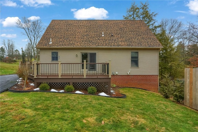 rear view of house with a deck, a yard, and roof with shingles