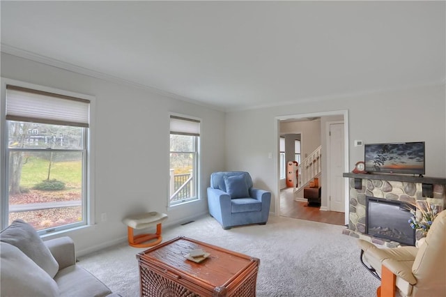 living area featuring stairs, a stone fireplace, carpet, and ornamental molding