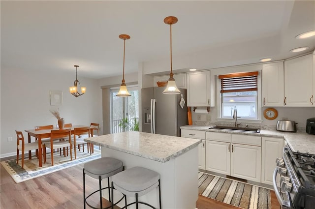 kitchen featuring light wood finished floors, stainless steel appliances, white cabinets, a sink, and a kitchen bar