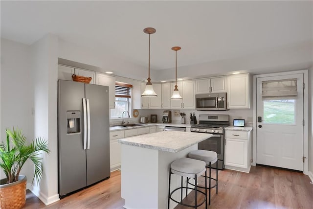 kitchen featuring white cabinets, appliances with stainless steel finishes, light countertops, light wood-type flooring, and a sink