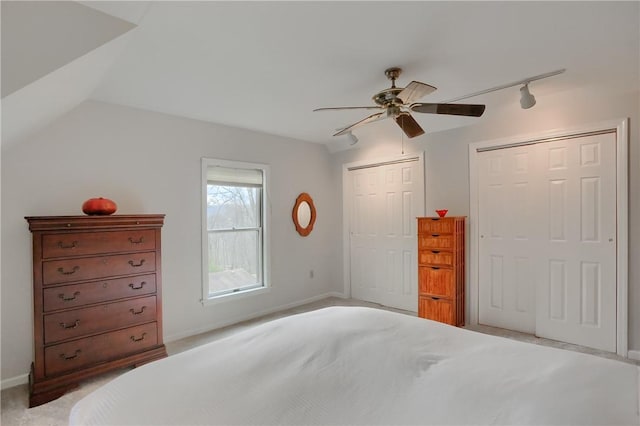 bedroom featuring two closets, lofted ceiling, a ceiling fan, light carpet, and track lighting