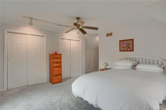 carpeted bedroom with rail lighting, visible vents, ceiling fan, and two closets