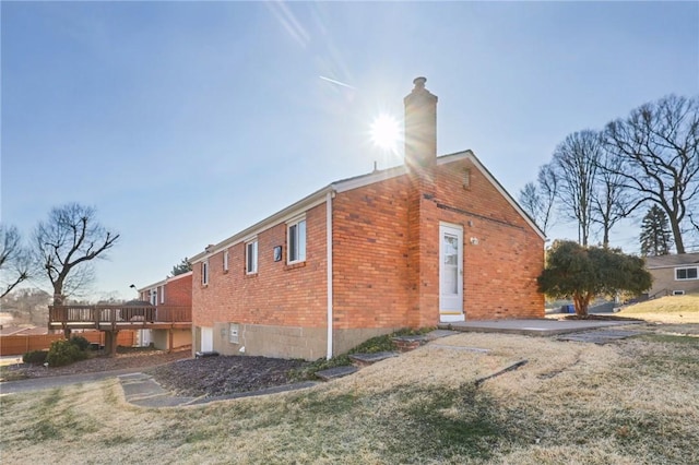 view of property exterior with a deck, a yard, brick siding, and a chimney