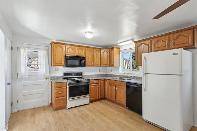 kitchen featuring light wood-style floors, brown cabinets, light stone countertops, black appliances, and a sink