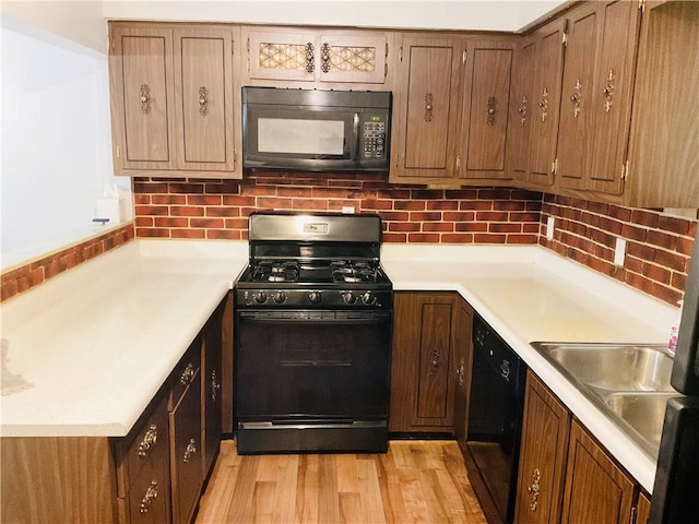 kitchen featuring a sink, light countertops, light wood-type flooring, backsplash, and black appliances