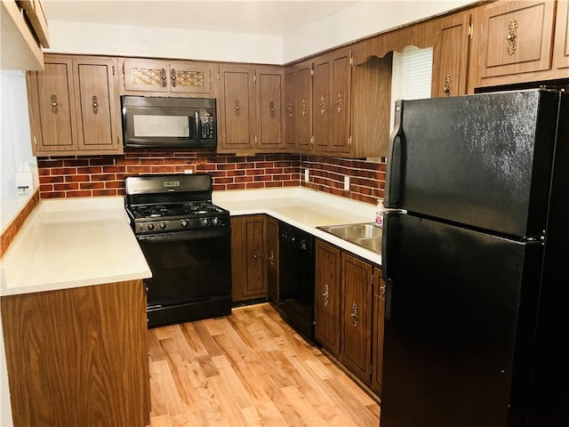 kitchen with light countertops, backsplash, light wood-style floors, a sink, and black appliances