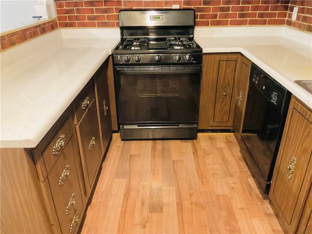 kitchen featuring brown cabinets, light countertops, decorative backsplash, light wood-type flooring, and black appliances