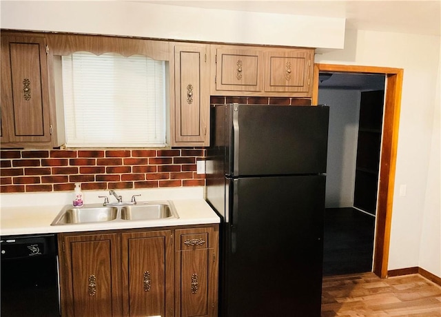 kitchen featuring baseboards, decorative backsplash, light countertops, black appliances, and a sink