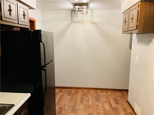 kitchen featuring light wood-style flooring, baseboards, light countertops, and freestanding refrigerator