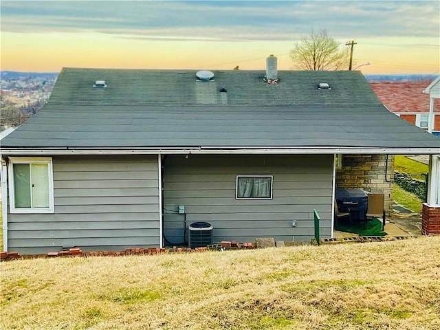 back of property at dusk with a lawn and central AC unit